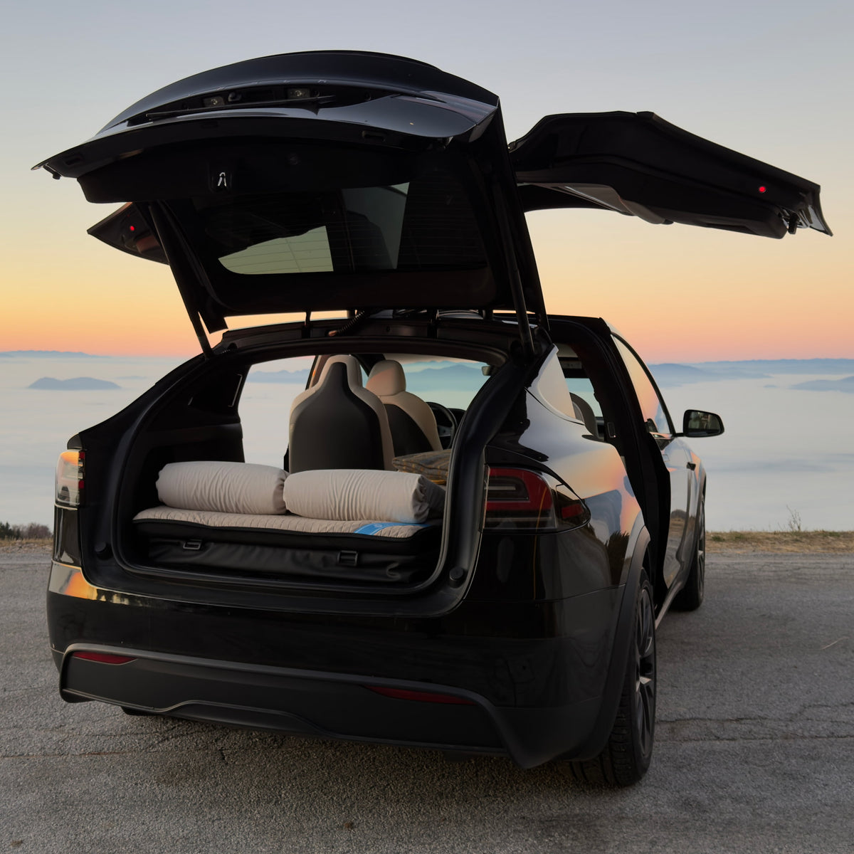 Dreamcase Model X 6-seater car bed mattress setup in open Tesla trunk with scenic mountain panorama