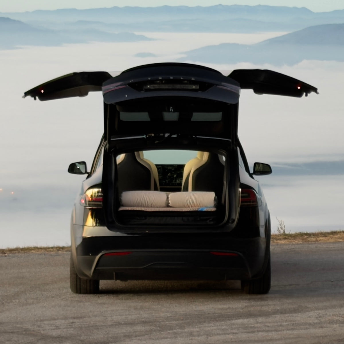 Dreamcase car bed mattress in open Tesla Model X trunk with misty mountain background
