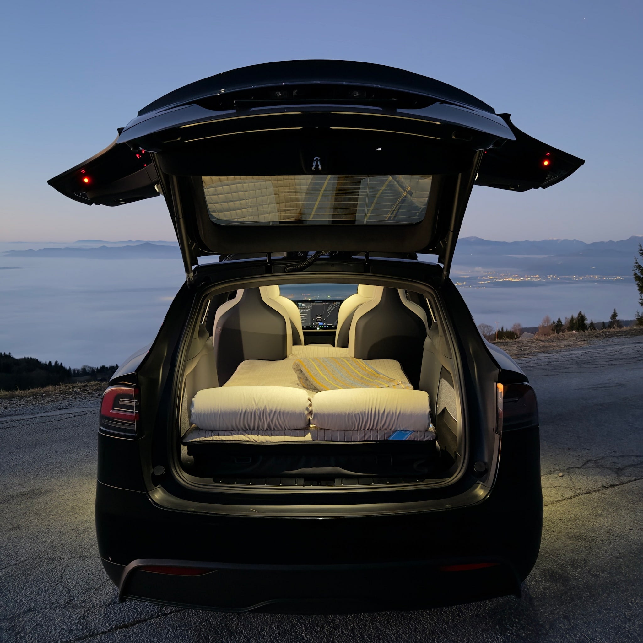Dreamcase car bed inside illuminated Tesla model X 6-seater trunk during night-time car camping