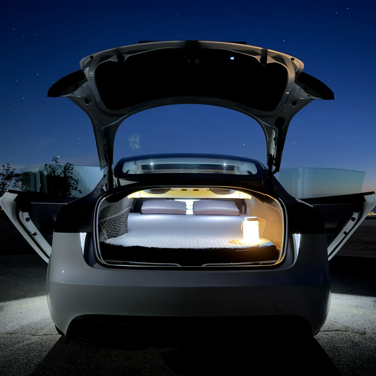 DreamCase Memory car bed in a Tesla Model 3 at night, rear hatch open with lantern on the mattress
