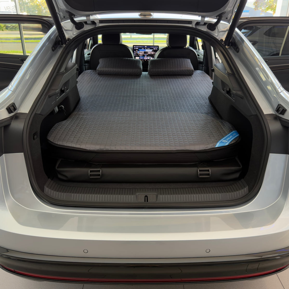 DreamCase Memory car bed fitted in a Volkswagen ID.7, rear hatch open, grey quilted mattress and pillows on the platform
