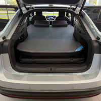 DreamCase Memory car bed fitted in a Volkswagen ID.7, rear hatch open, grey quilted mattress and pillows on the platform